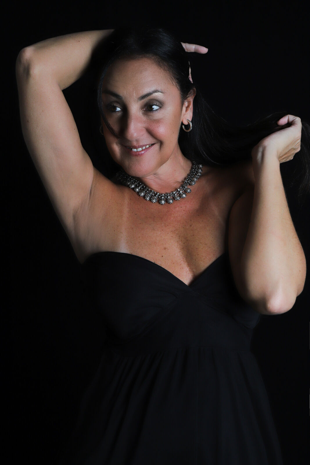 Renata Pacheco em pose de dança, braços erguidos, fundo escuro